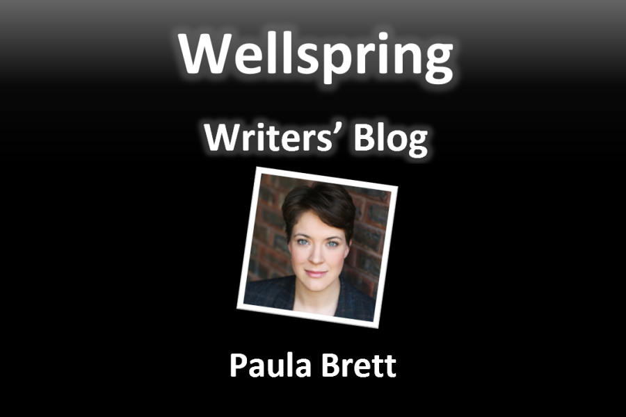 White letters on black background read 'Wellspring Writers' Blog'. Underneath a framed portrait photo of a white person looking directly to the camera. They have green eyes and very short brown hair. Underneath the photo the Paula Brett is written in white letters.