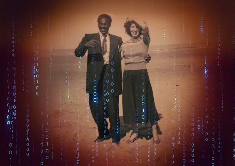 A joyful 50's style black and white photo of a mixed-race couple against a futuristic dark brown background with coding digits 0 and 1 appearing in repeated vertical sequences.. The photo in the middle shows a smart, suited Black man and a well-dressed White woman posing in the countryside. They tenderly hold each other, smiling at the camera.