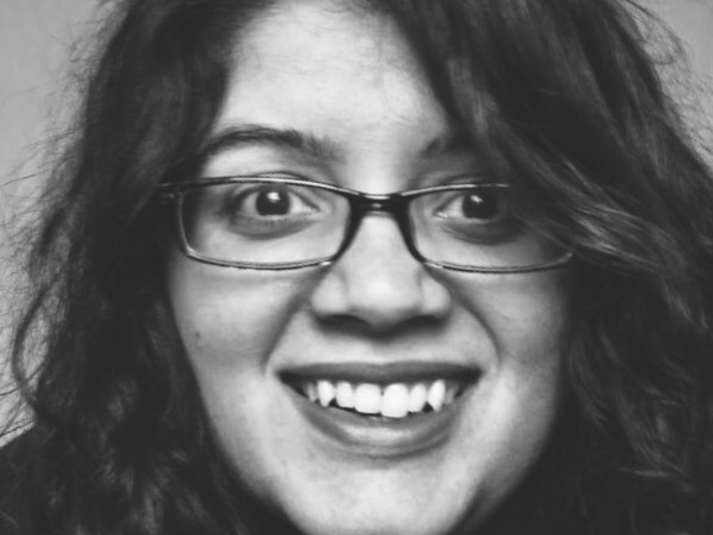 Black and white photo of a Kashmiri person with dark curly hair, glasses and a goofy grin.