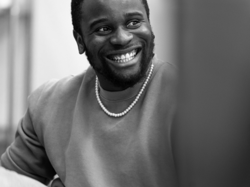 Black and white photo of a black man who is sitting down but you can't see the chair. he is not looking directly into the camera.
