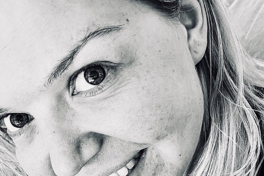 Black and white close-up photo of a white blonde woman. She looks to the camera and smiles cheerfully.