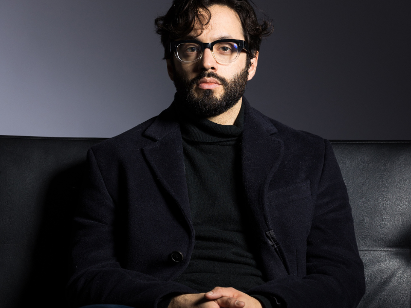 Man in his mid-thirties with olive skin, dark hair, short beard, and glasses.