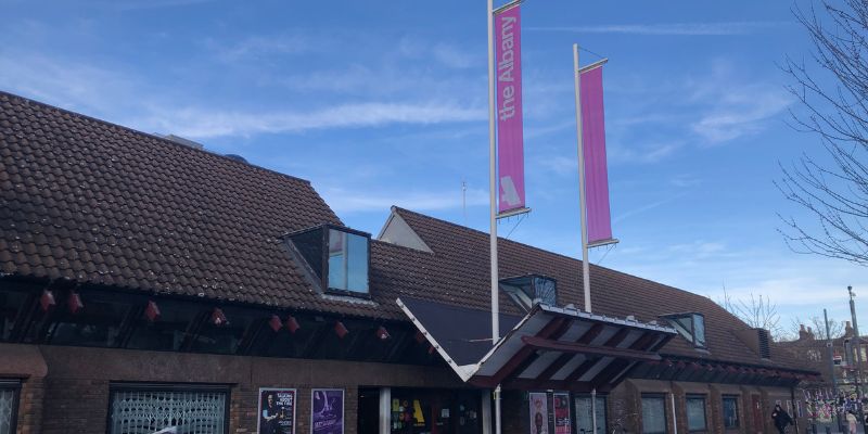A 1980s 2 storey building, with 2 pink flags outside, reading 'the Albany'.