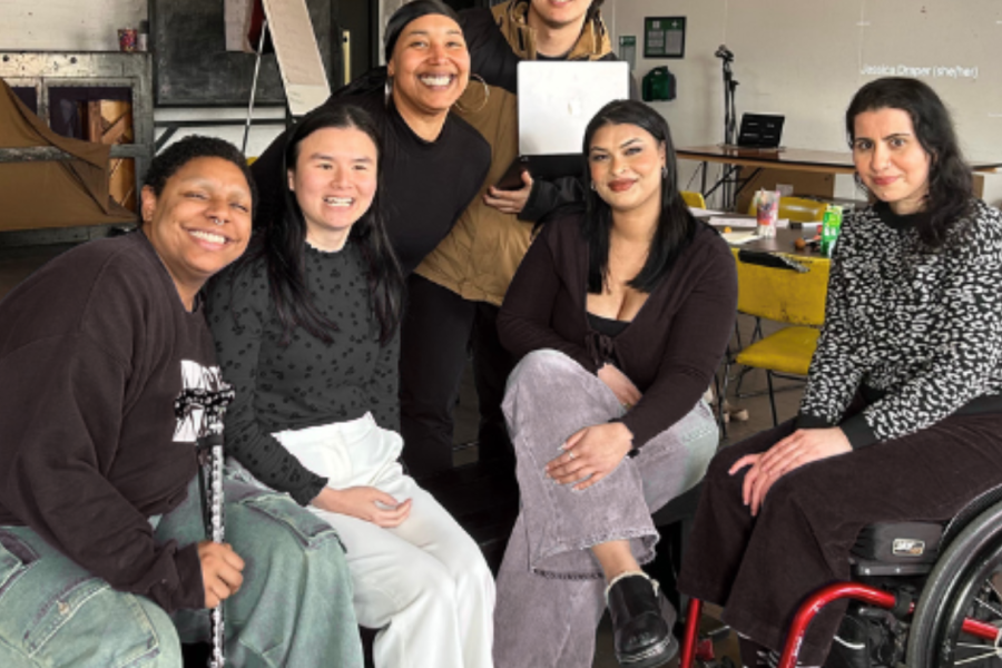 Six people, posing for a group photo, smiling. From left to right: Eli, a Black person with short hair, nose piercing and black and white stick. Jasmine, a woman of Chinese heritage wearing a bright blue jumper. Koko, a Black woman wearing large hoop earrings. Joey, a man of East Asian heritage, with short hair, holding a laptop. Arielle, a woman of African diaspora heritage, with long dark hair and blue jeans. Dalia, a woman of Egyptian-American heritage wearing a black and white jumper and using a black wheelchair.