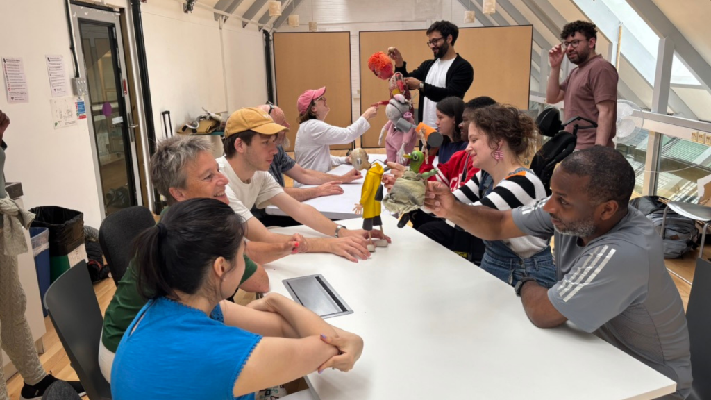 Eleven people sit around two tables, holding and handling puppets, or touching the puppets.