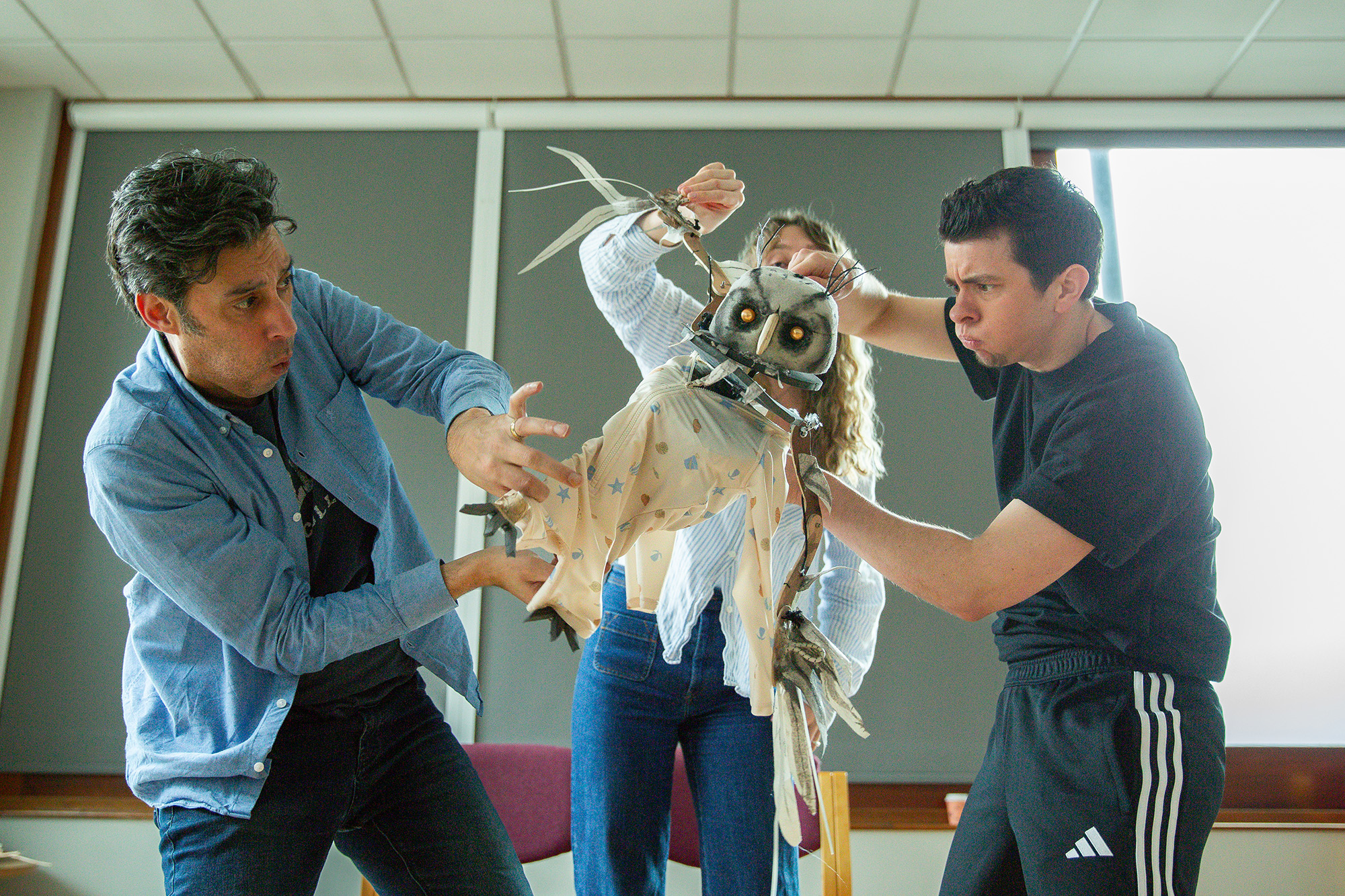 Three people intensely manipulate a detailed owl puppet with feathered wings in a brightly lit room, working together to animate its movements.